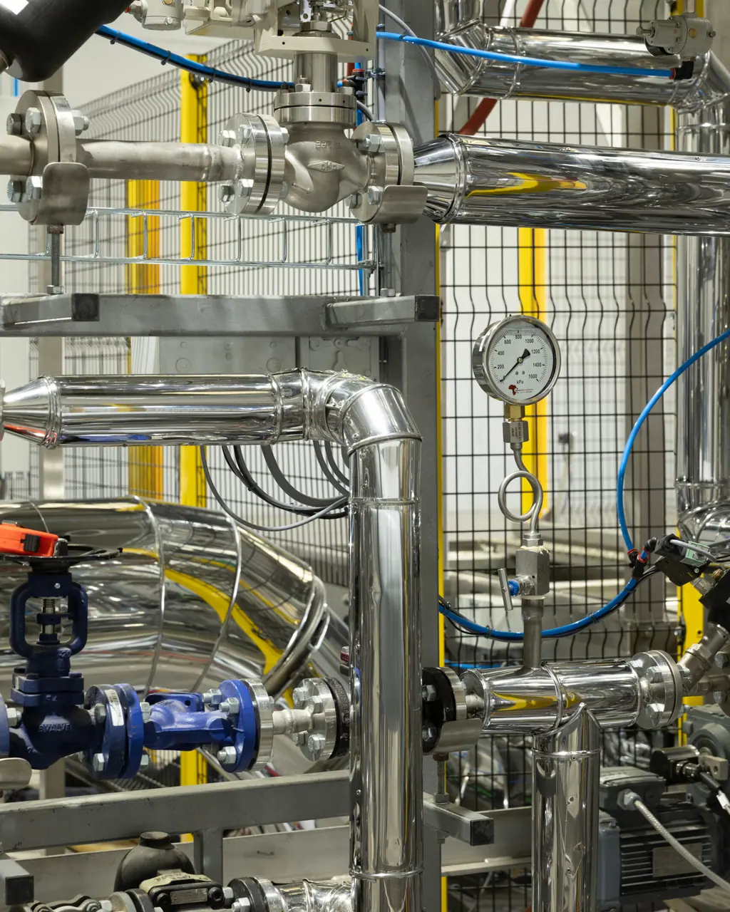 A close view of the steam manifold: flanged stainless pipework, hand valves, and a pressure gauge reading in kilopascals.